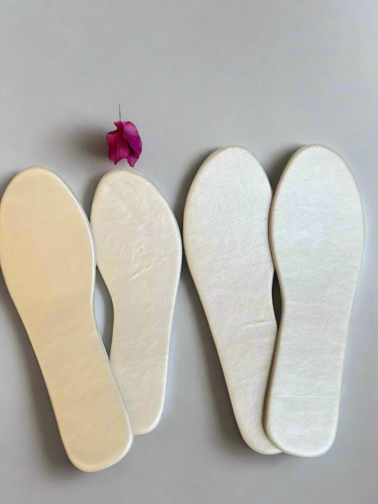Two pairs of white shoe insoles on a textured surface with a pink flower.