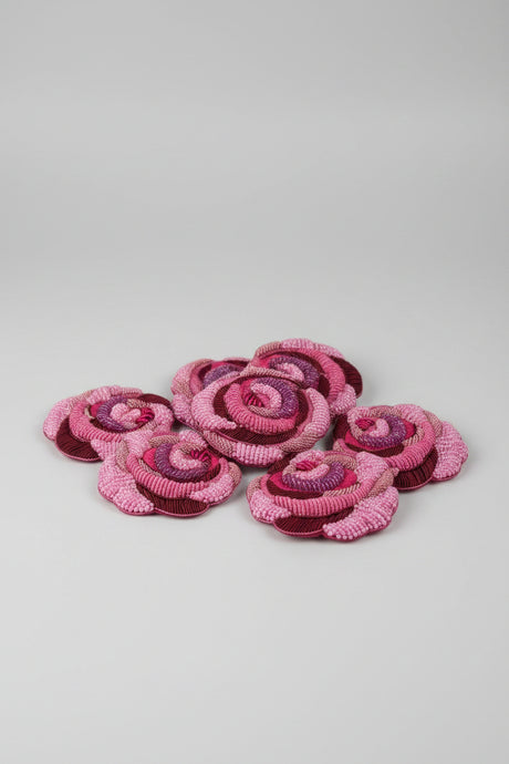 A set of handmade fabric rose embellishments in shades of pink, magenta, and deep burgundy, arranged on a wooden tabletop.