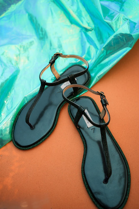Pair of green sandals on a reflective orange and blue surface