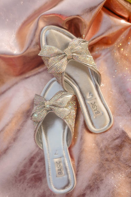 Gold sandals with bow details on a pink fabric background